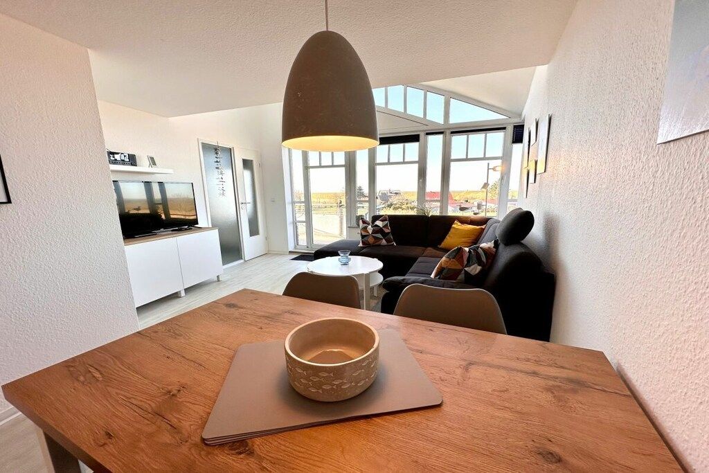 Una sala de estar moderna con una mesa de comedor de madera, un sofá y un ventanal con vistas al exterior.