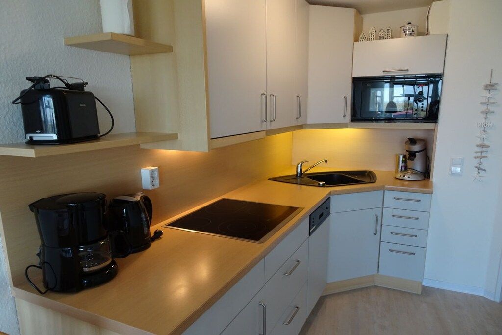 Una cocina compacta con microondas integrado, cafetera y lavamanos.