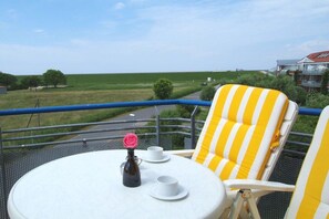 Een balkon met een tafel, stoelen en uitzicht op een groen veld.