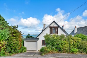 Ein weißes Haus mit Garage, umgeben von viel Grün, mit Blick auf das Meer im Hintergrund.