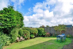 Ein gepflegter Garten mit Holzzaun, Rasen und einem Tisch mit Stühlen.