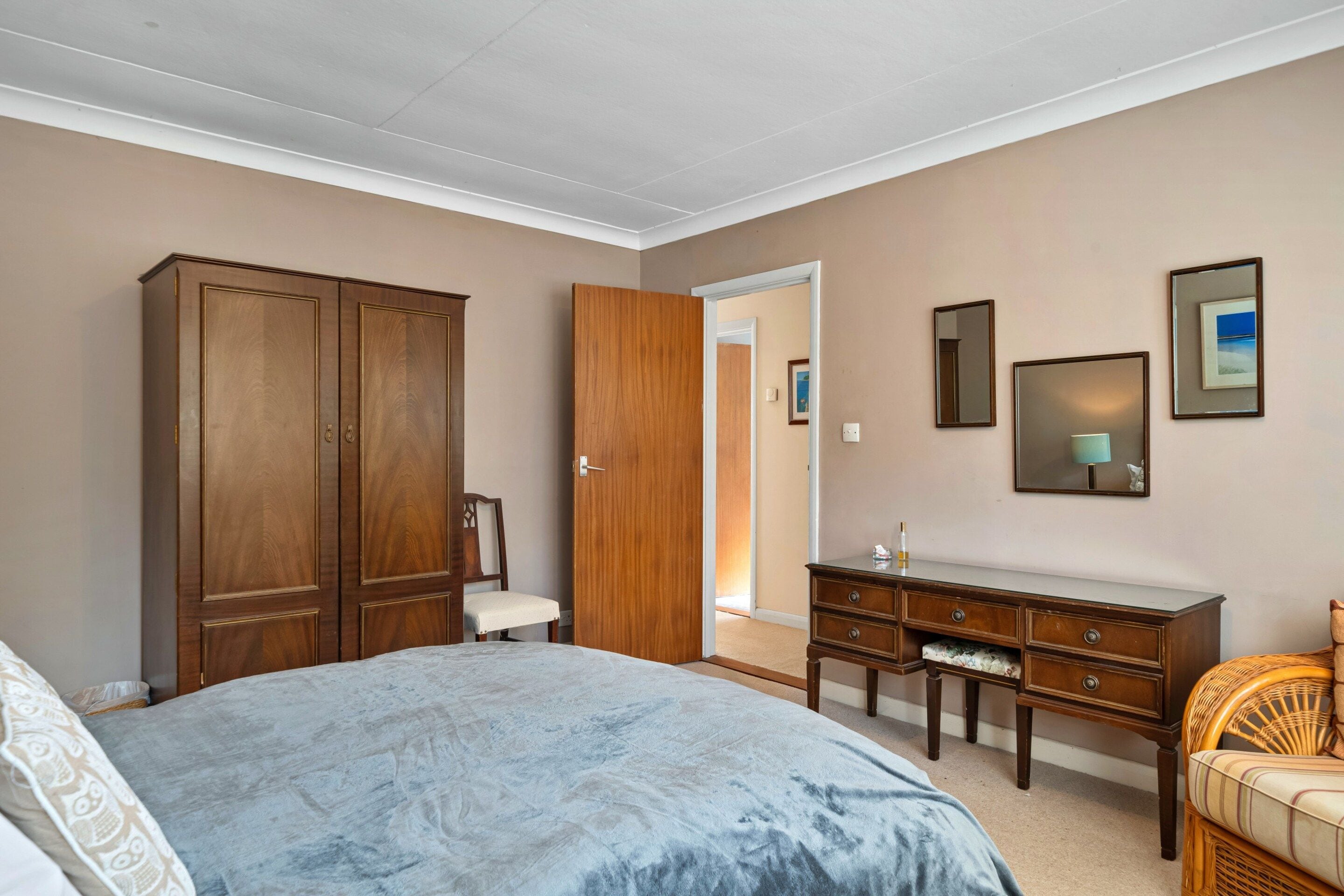 Un dormitorio con cama, armario, cómoda, silla y puerta que da a otra habitación.