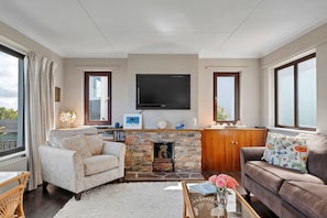Ein Wohnzimmer mit Kamin aus Stein, einem flachbildfernseher darüber und einer gemütlichen Sitzecke mit Sofa und Sesseln.