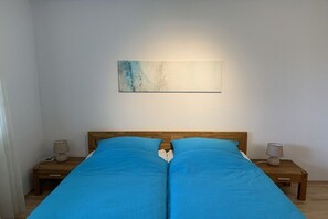 A double bed with a wooden headboard, two bedside tables with lamps, and a wall-mounted abstract painting. - Holiday apartment with 1 bedroom (Bad Honnef)