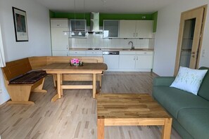 A compact living space with a kitchenette, a dining area with a wooden table and bench, and a green sofa. - Holiday apartment with 1 bedroom (Bad Honnef)