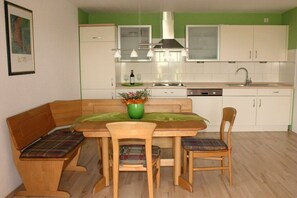 Een kleine keuken met een eettafel, stoelen en een groene vaas.