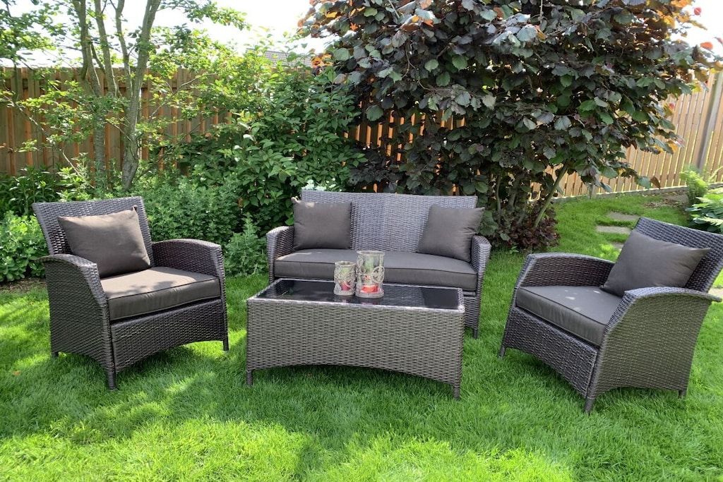 Een patio met rieten meubilair, waaronder twee stoelen en een bank, en een bijzettafeltje met decoratieve objecten.