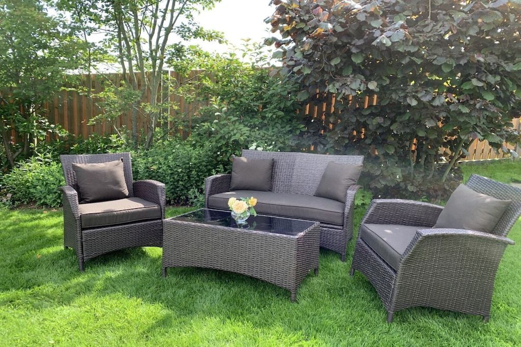 Un patio amueblado con mobiliario de mimbre, incluyendo dos sillones y un sofá, además de una mesa de centro de vidrio.