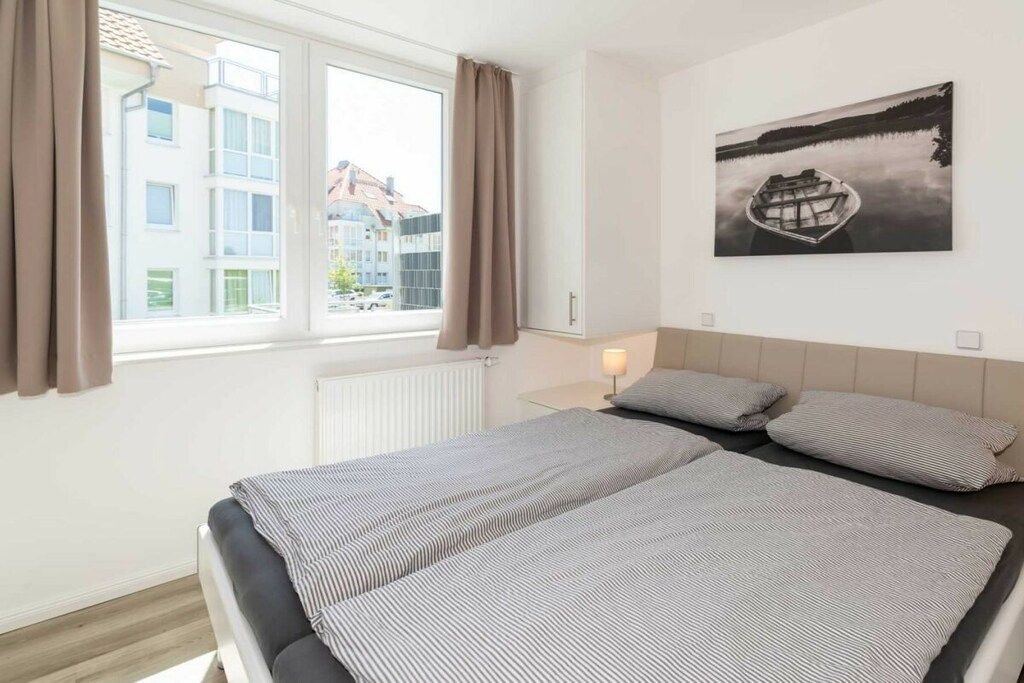 Una habitación de hotel con cama, ventana con cortinas, un cuadro en la pared y un radiador.