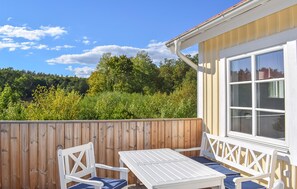 A wooden deck with a white table and two chairs, a window with a checkered curtain, and a view of a forested area. - 1 bedroom pet friendly home in Trensum (Trensum)