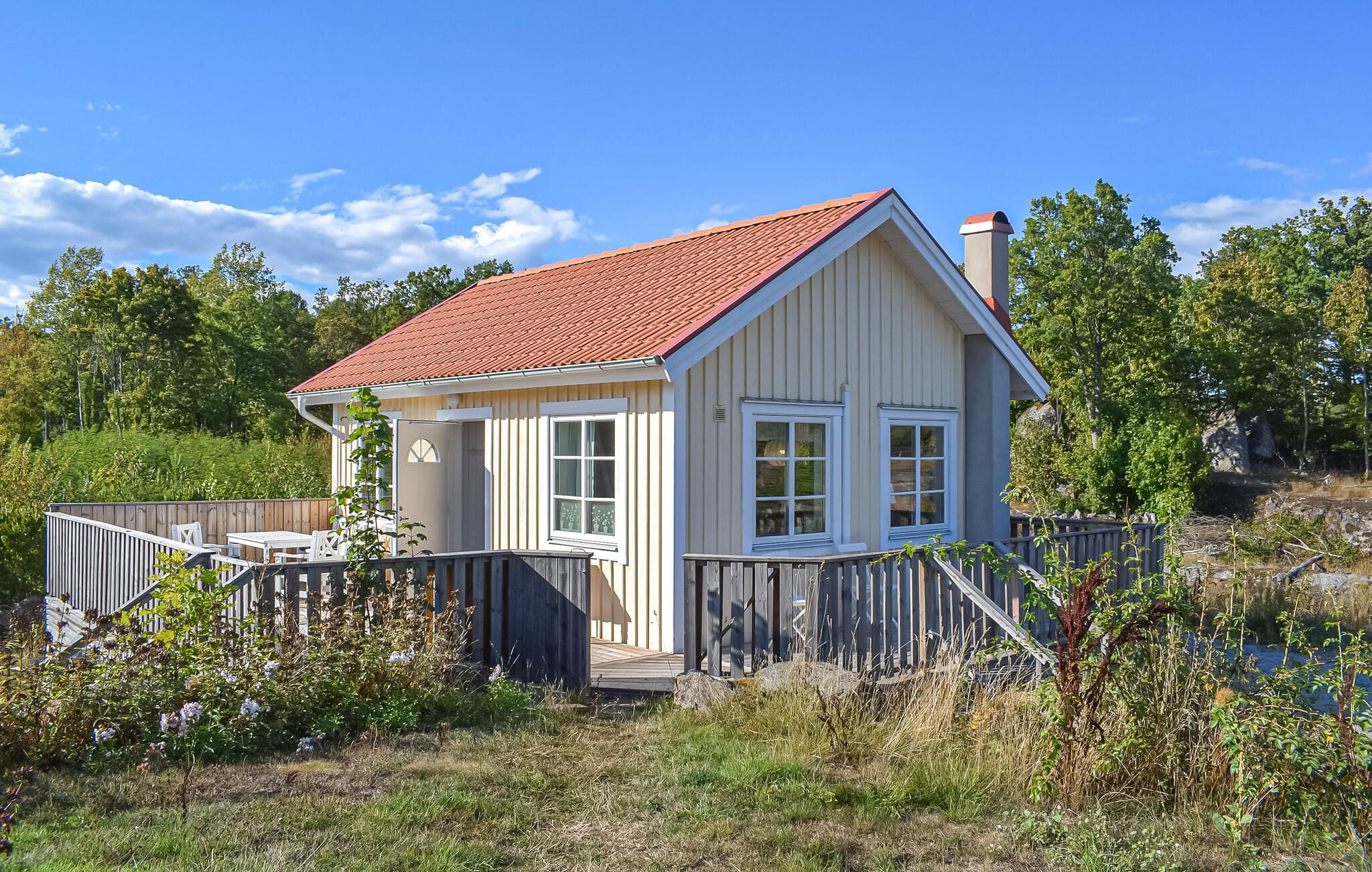Une maison de plain-pied avec un toit recouvert de tuiles rouges, un porche à l’avant et une terrasse en bois.