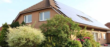 A house with a sloped roof, solar panels, and a well-maintained garden with various shrubs and a small tree.
