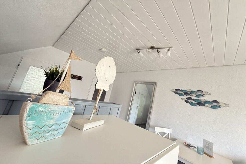Ein Zimmer mit weißer Decke, einem weißen Tisch, einem weißen Stuhl, einer Wand mit Fischmotiv und einer Tür.