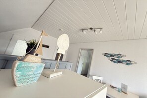 A room with a white ceiling, a white table, a white chair, a wall with a fish decoration, and a door. - Friesenkoje Horumersiel - bunk 3 (Wangerland)
