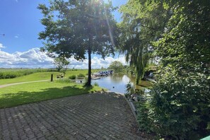 A paved walkway beside a calm water body, surrounded by lush greenery and trees. - Holiday apartment with 2 bedrooms (Pilsum)