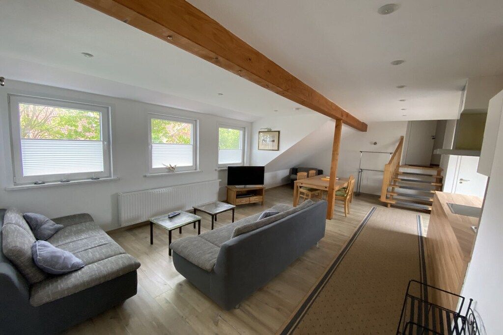 Ein modernes Wohnzimmer mit Sofa, Fernseher und Essbereich, mit schräg versiegelter Decke und Holzbalken.