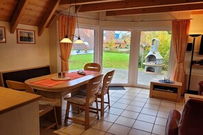 A dining area with a wooden table, chairs, and a view of a garden and outdoor grill. - Holiday home with 3 bedrooms (Wurster-Nordseeküste\/ Dorum-Neufeld)