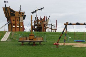 Une aire de jeux dotée d’une structure ludique sur le thème des pirates, comprenant des toboggans et des balançoires.