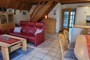 A cozy living room with a red leather sofa, wooden dining table, and a kitchen area with cabinets and a refrigerator. - Holiday home with 3 bedrooms (Wurster-Nordseeküste\/ Dorum-Neufeld)