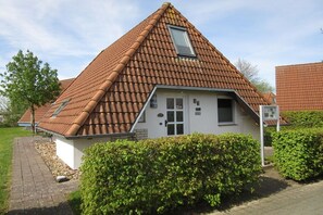 A house with a sloped roof, a small attached garage, and a well-maintained hedge in front. - Holiday home with 3 bedrooms (Wurster-Nordseeküste\/ Dorum-Neufeld)