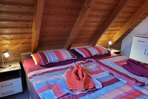 Une chambre avec deux lits, des poutres apparentes en bois au plafond, une table de chevet avec une lampe et une armoire blanche.