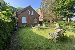 A brick house with a lawn, outdoor furniture, and a garden. - Holiday home with 1 bedroom (Krummhörn)