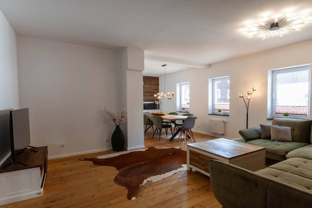 Un salon moderne avec un canapé, une table basse et un téléviseur. On aperçoit à l’arrière-plan un coin repas avec des chaises et une table.