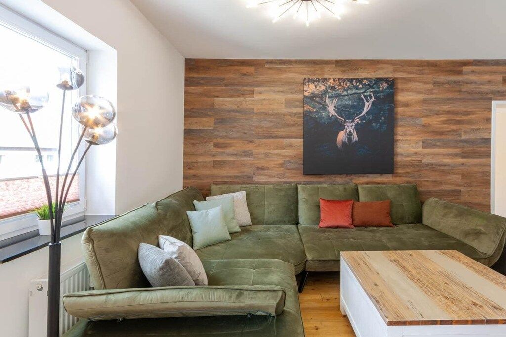 A modern living room with a green sectional sofa, a wooden coffee table, and a wall-mounted painting of a deer.