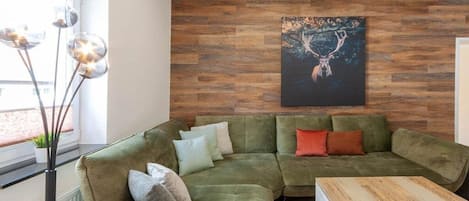 A modern living room with a green sectional sofa, a wooden coffee table, and a wall-mounted painting of a deer.
