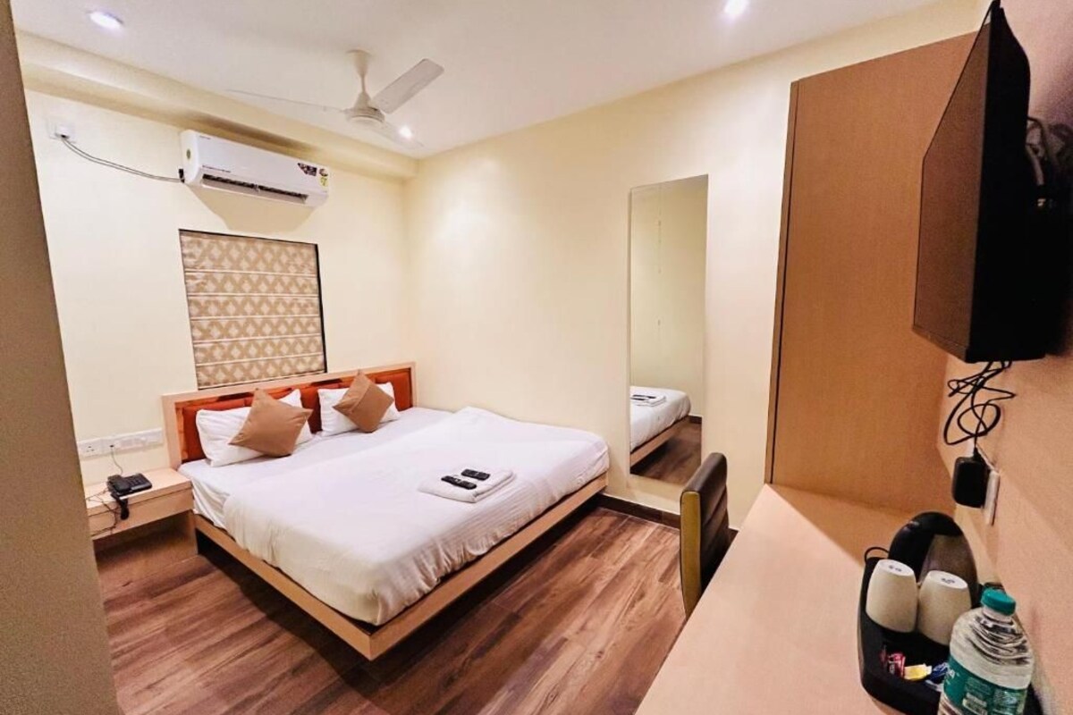 A hotel room with a bed, bedside table, nightstand, wall-mounted TV, and a mirror.