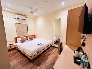 A hotel room with a bed, bedside table, nightstand, wall-mounted TV, and a mirror. - Hotel Golden Square (Kolkata)