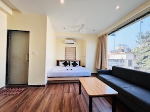 Una habitación de hotel con una cama, un sofá, una mesa de madera y un ventanal grande.
