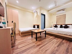 A hotel room with a wooden floor, a desk, two beds, a chair, and a wardrobe. - Hotel Golden Square (Kolkata)
