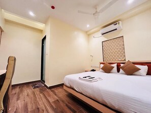 Habitación de hotel con una cama, un escritorio, una silla y un ventilador de techo.