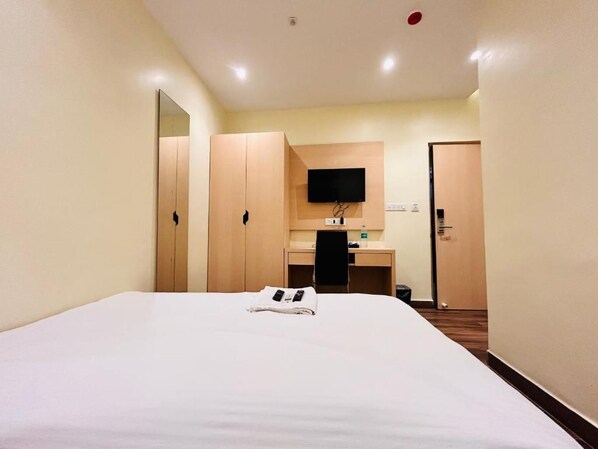 Habitación de hotel con cama, escritorio, silla, televisor y armario.