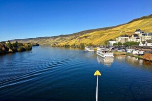 A river with boats, a town on the riverbank, and a hill in the background. - "Bernkastel Moselle Panorama" (Bernkasel-Kues)