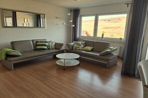 A living room with a sectional sofa, a coffee table, and a view of a desert landscape through a window. - "Bernkastel Moselle Panorama" (Bernkasel-Kues)
