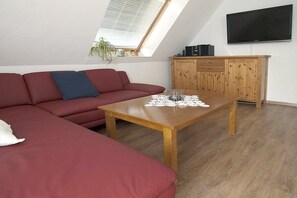 A living room with a red sofa, a wooden coffee table, a television mounted on the wall, and a wooden cabinet. - House Bekaan on the south beach - attic (Borkum)