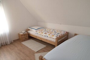 A bedroom with a single bed, a nightstand, a bedside table, and a window with curtains. - House Bekaan on the south beach - attic (Borkum)