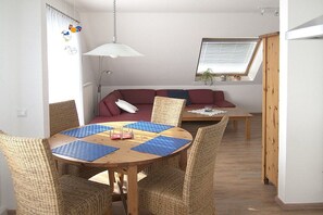 Ein Essbereich mit einem runden Tisch, Korbstühlen und einer Deckenleuchte.