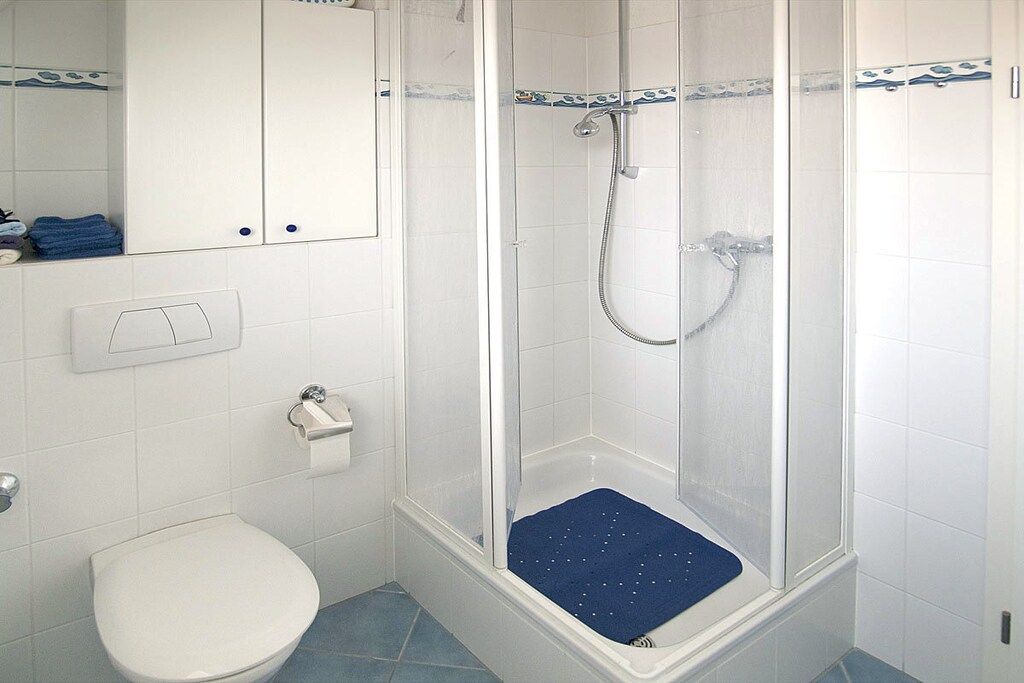 Et badeværelse med toilet, brusebad med blå måtte og hvid vask.