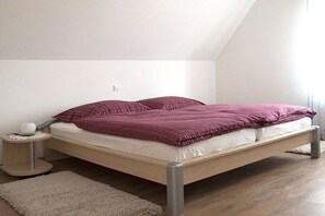 Ein Einzelbett mit Kopfteil, ein Nachttisch mit Lampe und ein kleiner Teppich auf Holzboden.