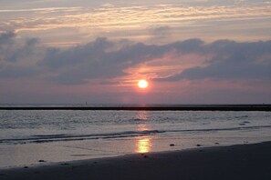 A sunset over a beach with calm waters and a clear horizon. - House Bekaan on the south beach - attic (Borkum)
