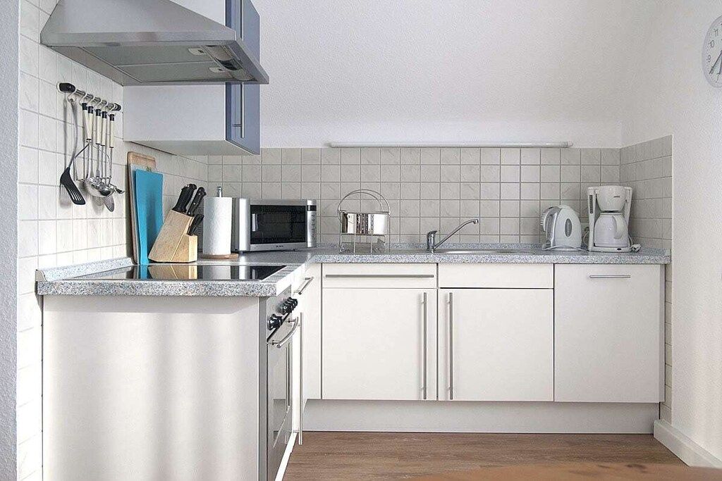 Une cuisine moderne avec des meubles blancs, un four à micro-ondes, une machine à café et un évier.