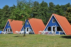 Three triangular-roofed cabins with white railings, a small table, and chairs outside. - Holiday island Tietzowsee - Finnish house (Zechlinerhütte)