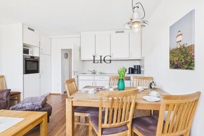 A modern kitchen with white cabinets, a dining area with wooden furniture, and a painting on the wall. - Holiday apartment Uhlenkamp 4 (Langeoog)