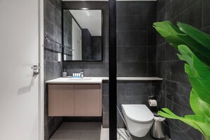 Een moderne badkamer met een grote spiegel, een wastafel met toiletartikelen, een toilet en een prullenbak.