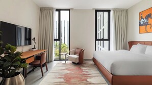 Una habitación de hotel moderna con cama, escritorio, silla y un ventanal grande.