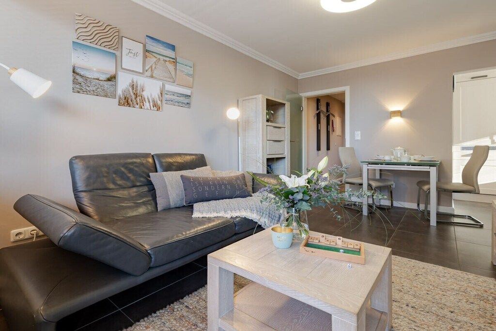 Una sala de estar moderna con un sofá de cuero, una mesa de centro de madera y un comedor con una mesa y sillas blancas.