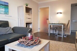 A modern living room with a sofa, coffee table, and a dining area with chairs. - Margarethenstraße Holiday Apartment 10 (Sylt\/Westerland)